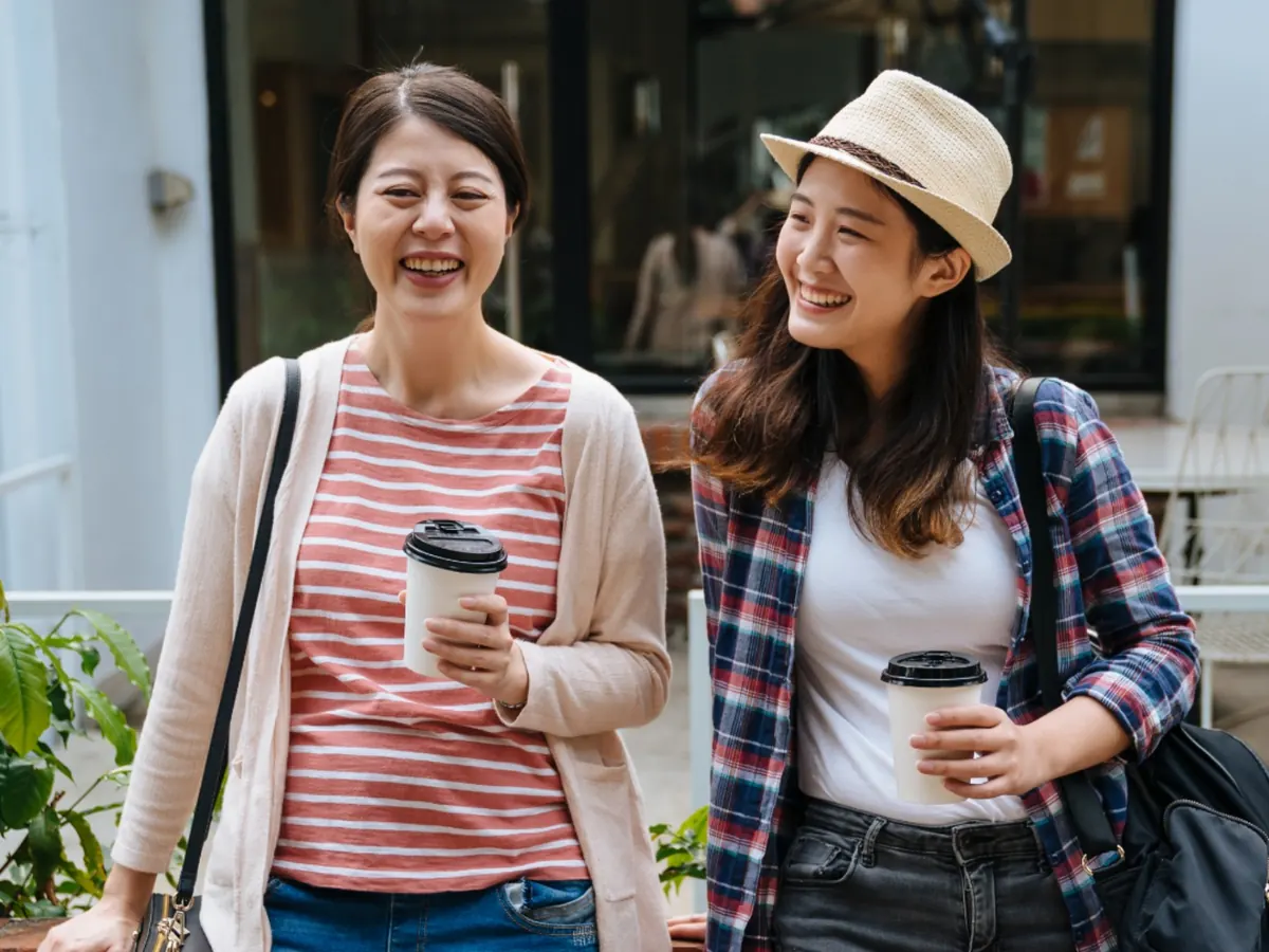 야외에서 두 여성이 커피를 들고 웃는 모습